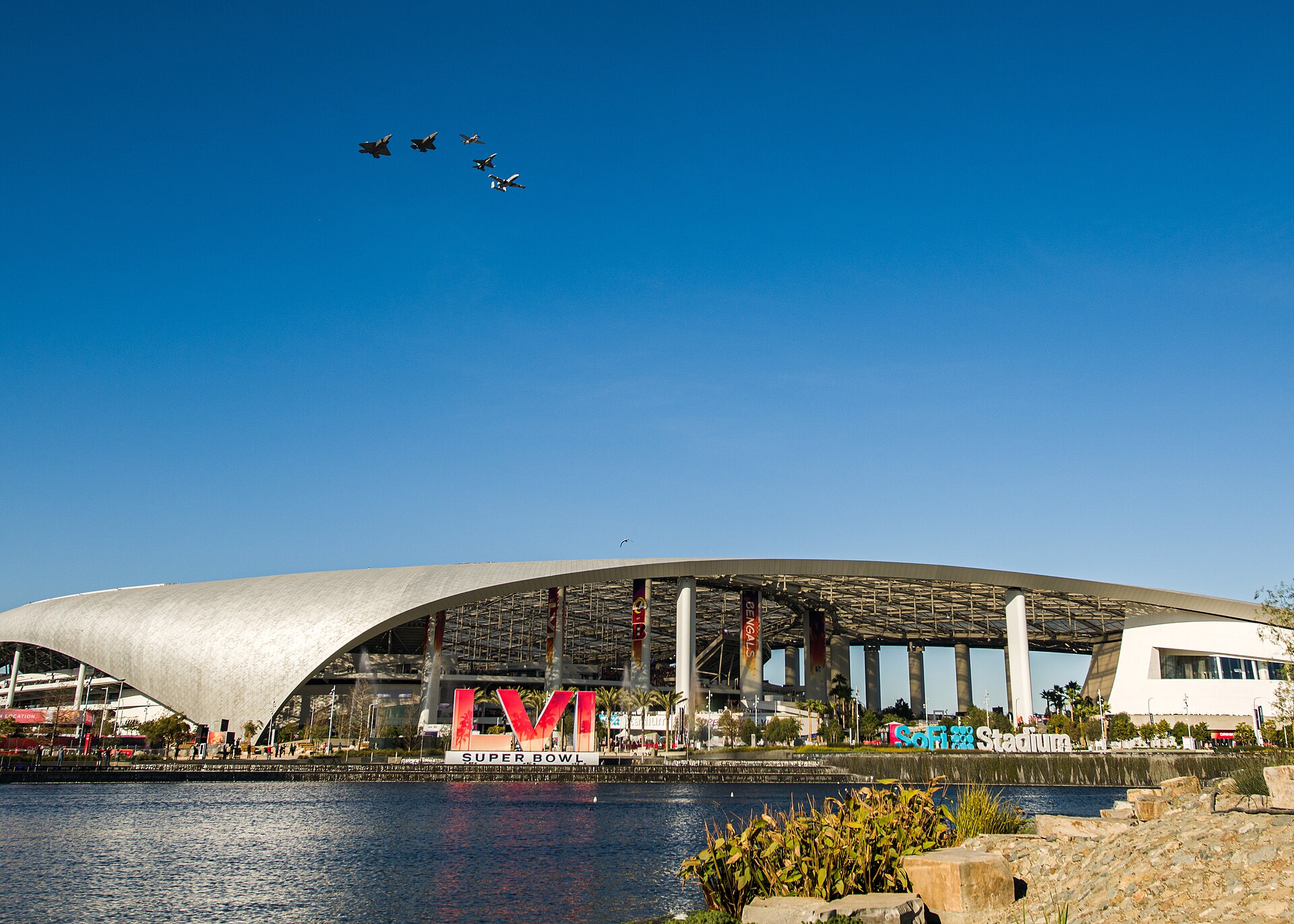 Military aircraft flying in formation over SoFi Stadium, with the large Super Bowl LVI sign in front of the stadium